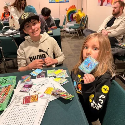 Two kids with Pokémon cards and coloring pages at the Kid Corner table