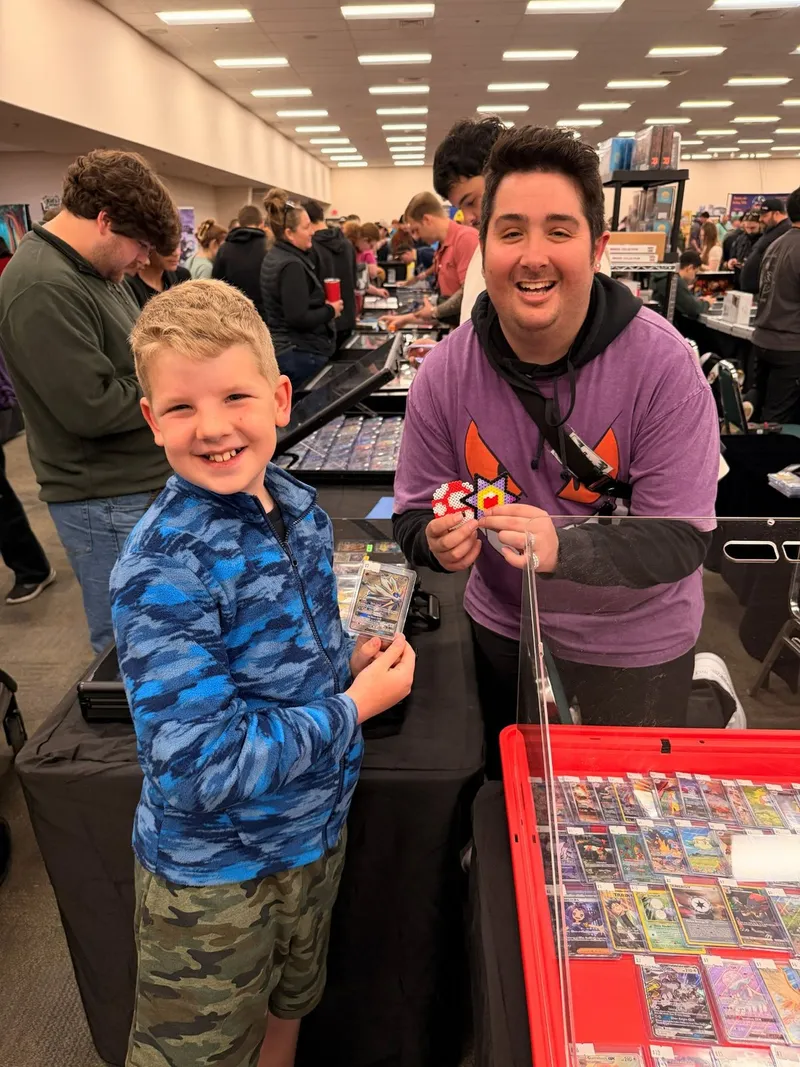 A kid showing off a new Pokémon card beside a smiling vendor