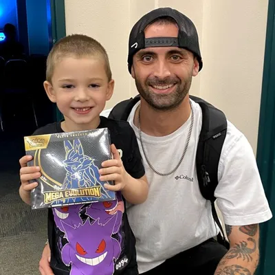 A young raffle winner and his dad with a sealed Pokémon Elite Trainer Box